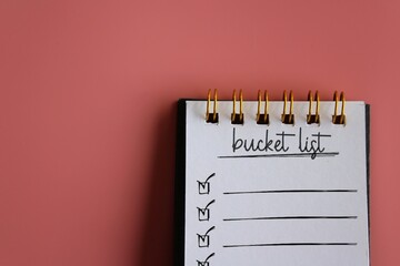 Top view image of notebook with text BUCKET LIST on pink background with copy space.