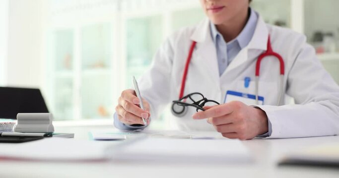 Female doctor sits at table, makes notes in paper ledger and prescribes treatment