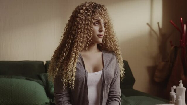 Young transsexual woman sitting on bed with pensive expression. Cinematic 4k.