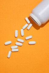 The white tablets were poured into an orange background from an unlabeled medicine bottle. Copy space for new drug advertising. Medical theme.