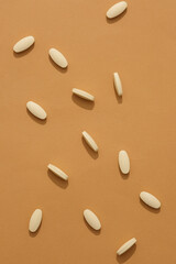 White tablets are randomly arranged on a brown background. Tablets are the form of oral medication most commonly prescribed by doctors to patients.