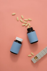 View from above of two unlabeled medicine bottles, tablets and a daily pill box on a pink background. Space for advertising western medicine.