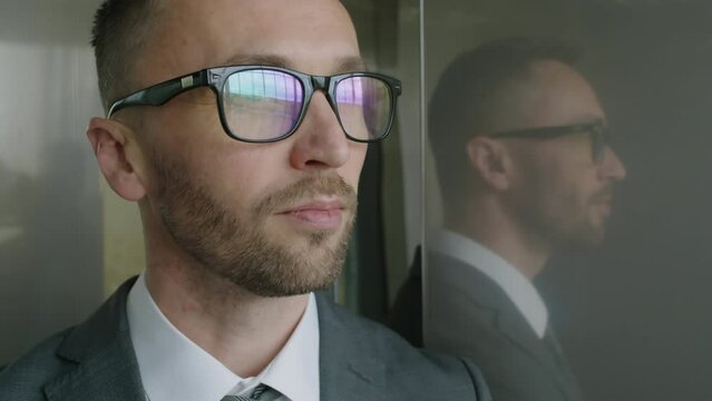 Close up of serious Caucasian businessman in glasses going up in elevator and looking away in modern office