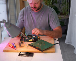 A man holds a soldering iron in his hand and solders a microcircuit