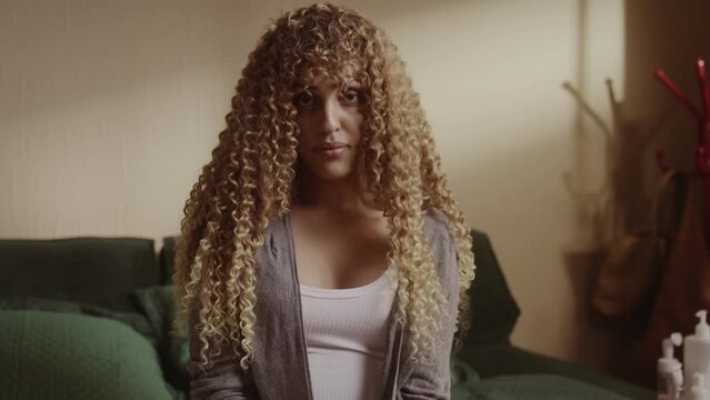 Mulher transexual jovem sentada na cama com expressao seria. Cinematico 4k.