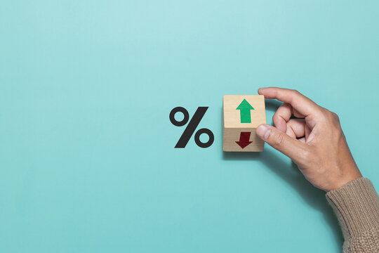 A man flip wooden cube with Down arrow to UP arrow and percentage symbol on green background. Concept of financial, stocks and interest rate