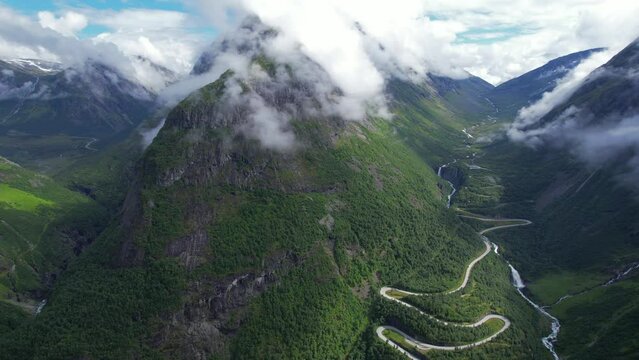 Aerial cinematic flyover view from above the clouds of the road and river in the valley of Videseter descending towards fjord in Norway