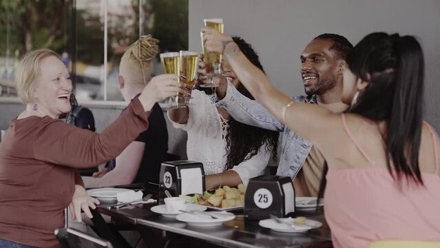 Grupo de diferentes idades brindando sentados em um bar ao ar livre. Cinematico 4k.