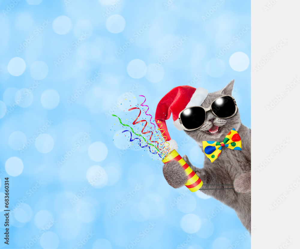 Aufkleber Happy cat wearing red santa hat and tie bow holds exploding firecracker and looks from behind empty white banner on blue festive background