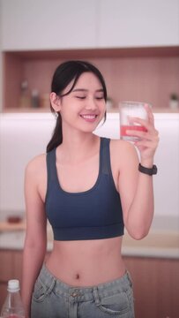 Asian sportswoman in sportswear sipping on a refreshing homemade fruit and vegetable drink in her kitchen. Prioritizing good health, she opts for nutritious food to maintain a positive body image