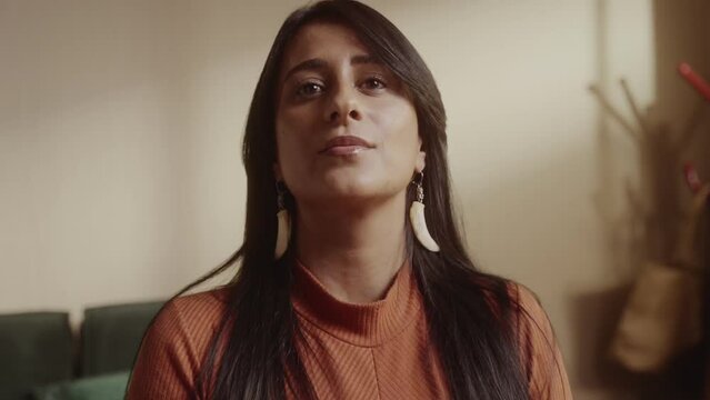 Woman of indigenous descent, sitting on bed with serious expression. Cinematic 4k.