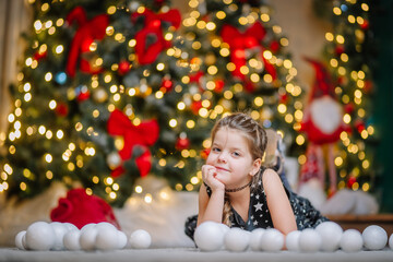 A little girl in a black dress with stars in a Christmas atmosphere. The girl is happy for Christmas. Christmas decorations.