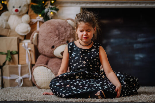 A little girl in a black dress with stars in a Christmas atmosphere. The girl is happy for Christmas. Christmas decorations. She is offended because she doesn't like taking pictures