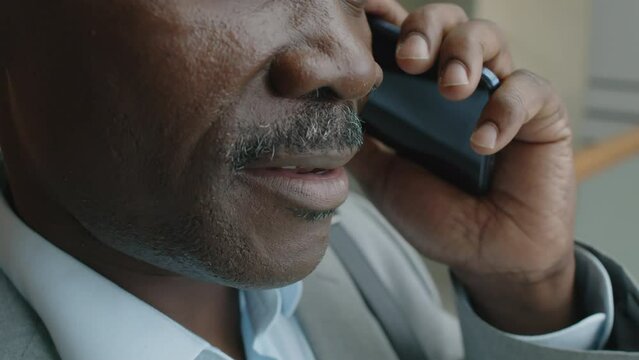 Tilt extreme closeup slowmo of Black man with moustache wearing suit and speaking on phone indoors