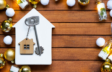 Key to house with a keychain tiny home on wooden background with Christmas decor layout. Gift for New Year, Christmas. Building, project, moving to new house, mortgage, rent and purchase real estate - obrazy, fototapety, plakaty