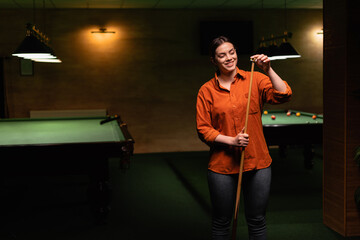 Attractive young woman chalking billiard cue while standing near pool table