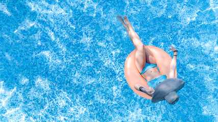 Beautiful woman in hat in swimming pool aerial drone view from above, young girl in bikini relaxes and swims on inflatable ring donut and has fun in water on tropical vacation on holiday resort
