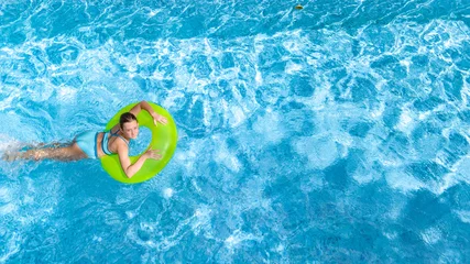 Fotobehang Active young girl in swimming pool aerial top view from above, teenager relaxes and swims on inflatable ring donut and has fun in water on family vacation, tropical holiday resort  © Iuliia Sokolovska
