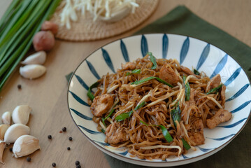 Traditional thai food, stir fried rice noodle with black sauce, chicken and vegetable on wooden table