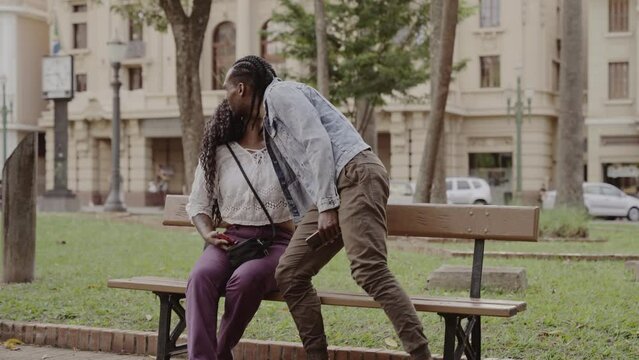 Young black friends, greeting with a kiss on the cheek, in the square on a sunny afternoon. Cinematic 4k.