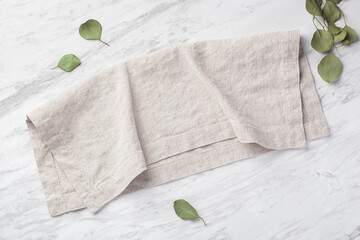 Natural linen napkin folded on marble kitchen table with green leaves