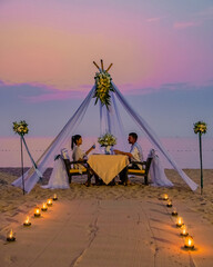 Romantic dinner on the beach in Phuket Thailand, couple man and woman mid age Asian woman and European man having dinner on the beach in Thailand during sunset. - obrazy, fototapety, plakaty