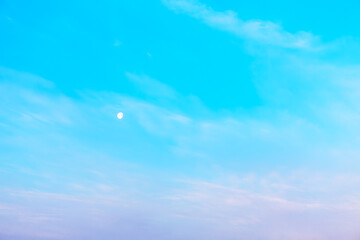 Blue sky background with tiny clouds and the moon in the evening