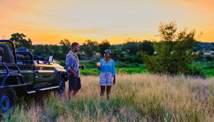 Asian women and European men on safari game drive in South Africa Kruger National Park. a couple of men and women on safari. Tourists in a jeep looking sunset with drinks on safari at a sundowner © Fokke Baarssen