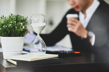 Hourglass on black office table with blurred businessman working on background. Time management...