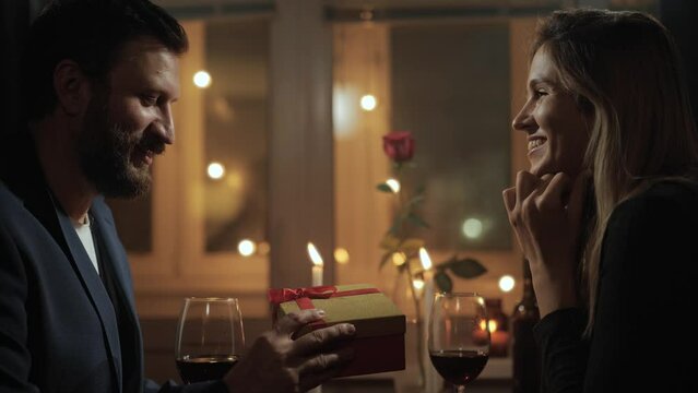 Gift, Valentines Day, wedding anniversary. Woman giving gift to man on date during romantic candlelight dinner