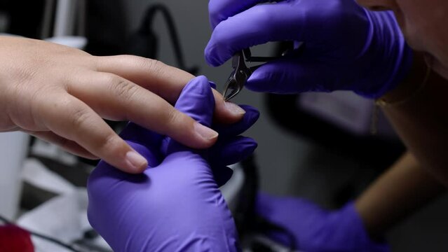A close up of manicurist treating a woman's cuticles using a nail scissors in a nail salon