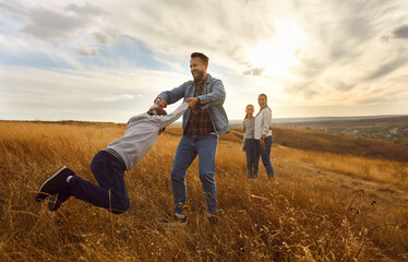 Happy parents with two kids walking together at sunset and having fun in the field. Young smiling father playing with his boy child outdoors. Family walk in nature and leisure concept.