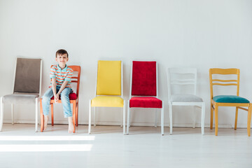 Fototapeta premium boy and many different chairs in the interior of a white room