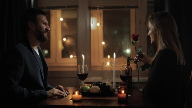 Date, Valentines Day, first date. Man gives one rose to woman during romantic candlelit dinner in restaurant or at home