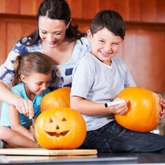 Halloween, pumpkin and a family in the kitchen of their home together for holiday celebration. Creative, smile or happy with a mother, son and daughter carving a face into a vegetable for decoration