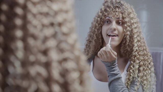 Linda mulher transexual de cabelos cacheados passando batom em frente ao espelho. Cinematico 4k.