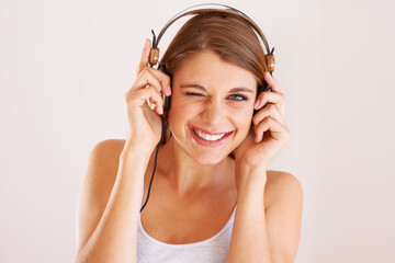 Woman, portrait and wink with headphones in studio for music, audio subscription or streaming...