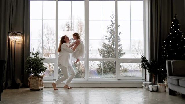 Mother and little daughter having fun together at Christmas morning. Happy family with big window at background. Christmas holidays concept. 4K, UHD