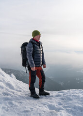  A middle-aged male tourist with a backpack over his shoulders stands on the edge of a mountain and...