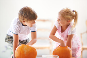 Halloween, happy and carving a pumpkin with children at a home table for fun and bonding. Boy and...