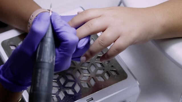A manicurist treats a woman's cuticles using a manicure machine in a nail salon