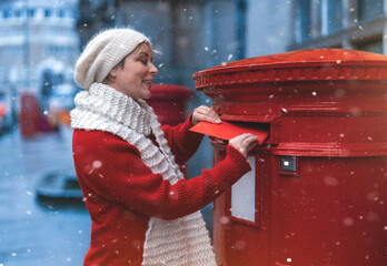 woman in a red coat  putting a card in the red postbox and walking around an English city on a snowy day - obrazy, fototapety, plakaty