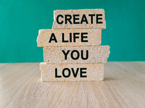 Motivational quote Create a life you love written on brick block. Beautiful wooden table green background. Business concept. Copy space.