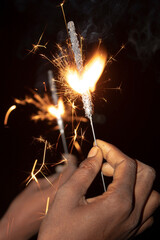 Close-up of woman's hands holding sparklers on black background