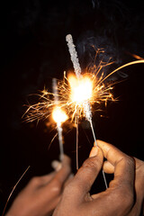 Close-up of woman hands holding sparklers on black background.