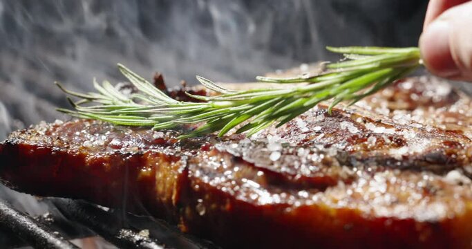 Appetizing juicy piece of steak seasoned with spices and rosemary leaves. Hot grill grate. Tongues of flame caress juicy piece of steak. Aromas of summer barbecues are in air. Copy space, close-up