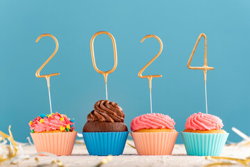 Holiday New Year muffins with pink butter cream and 2024 numbers on blue background.