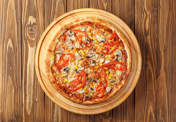 delicious pizza with chicken, mushrooms, cheese, tomatoes and corn on a wooden background