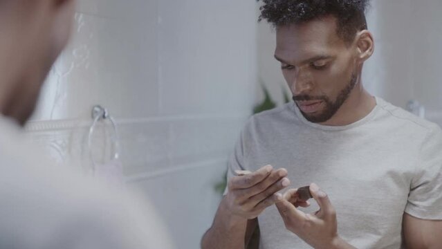 Homem bonito aplicando hidratante e olhando para si mesmo em pe na frente do espelho no banheiro. Cinematico 4k.