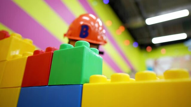 Handsome little boy dressed in a construction helmet plays big colored blocks. The child plays builder on the playground. Educational games for children.